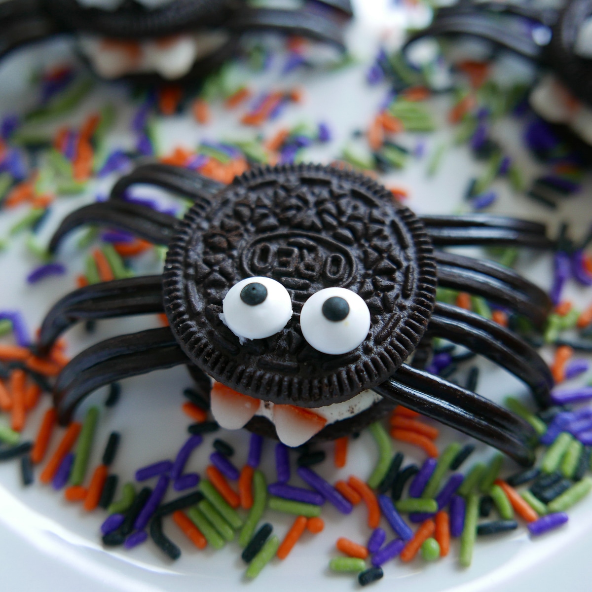 assembled spider cookie with legs, eyes, and candy fangs on a plate of halloween sprinkles.