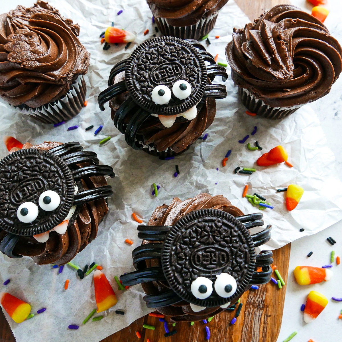 spider cookies on top of cupcakes on a candy decorated platter.