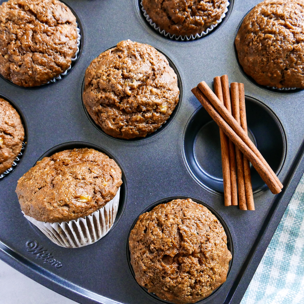 freshly baked muffins resting in a muffin tin with cinnamon sticks. 