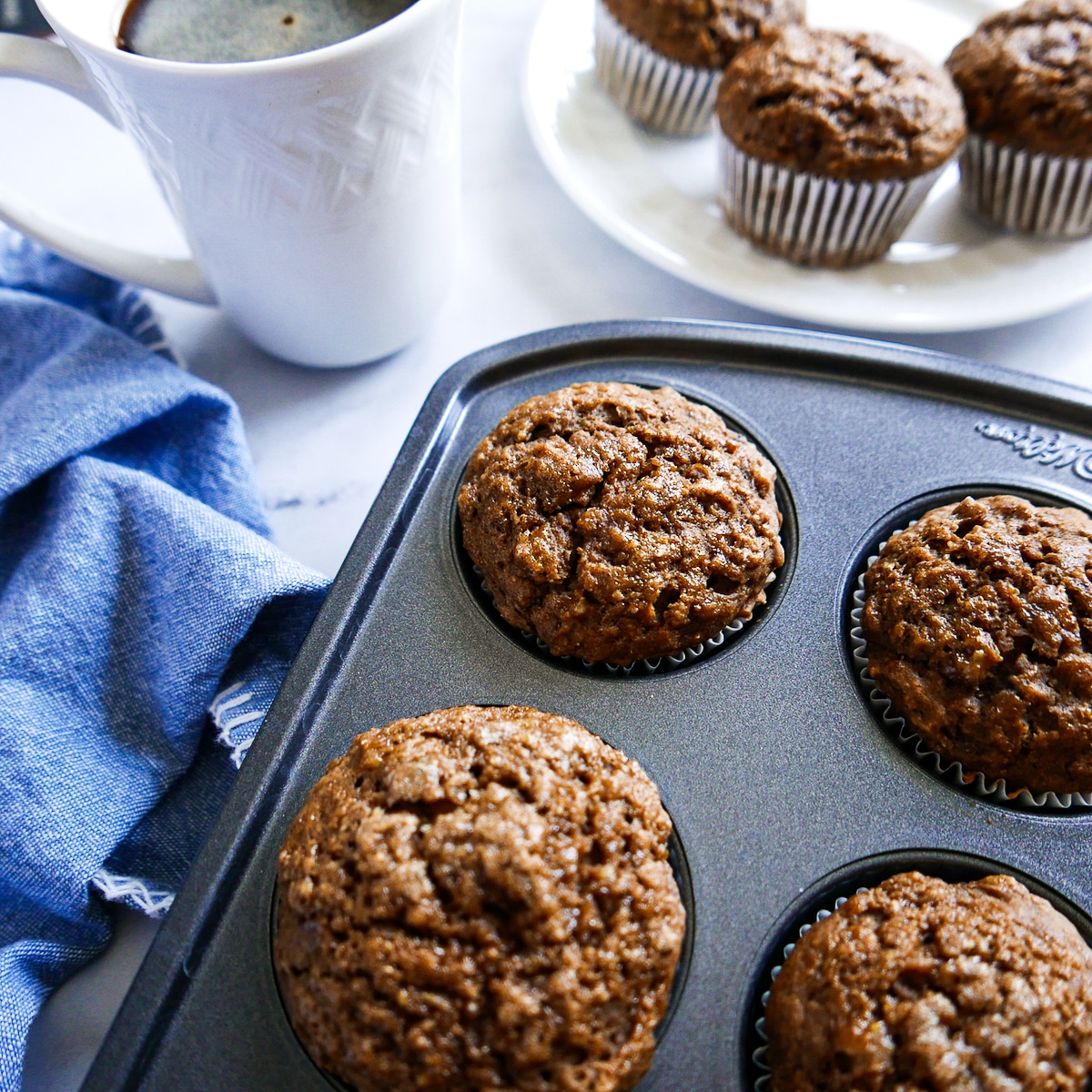 muffins in a muffin tin with a napkin and cup of coffee in the background.