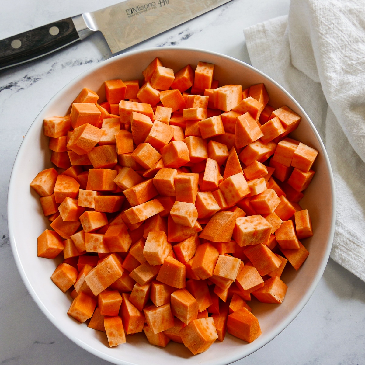 bowl of diced sweet potatoes with a chef's knife and white napkin.