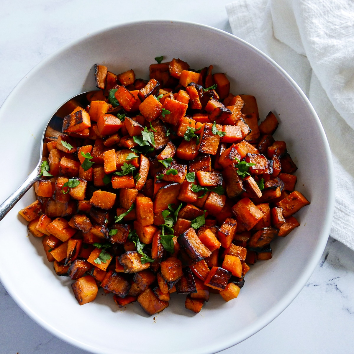 large white bowl of skillet sweet potatoes with a serving spoon. 