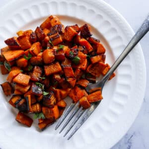 fork resting on a plate of sauteed sweet potatoes garnished with cilantro.