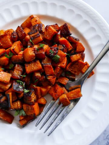 fork resting on a plate of sauteed sweet potatoes garnished with cilantro.