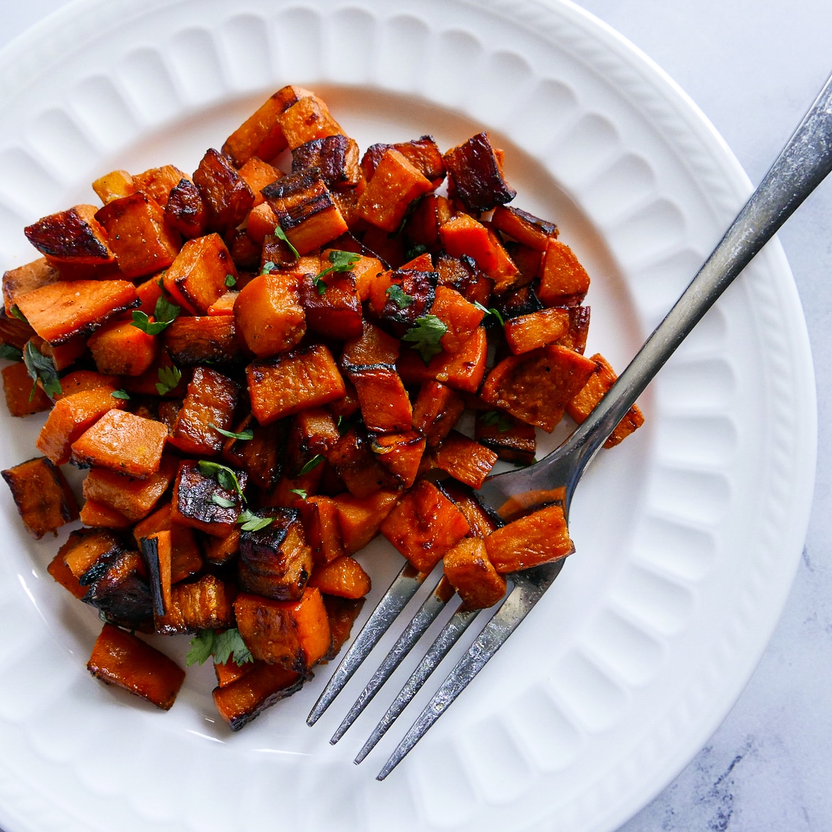 fork resting on a plate of pan-fried sweet potatoes garnished with cilantro.