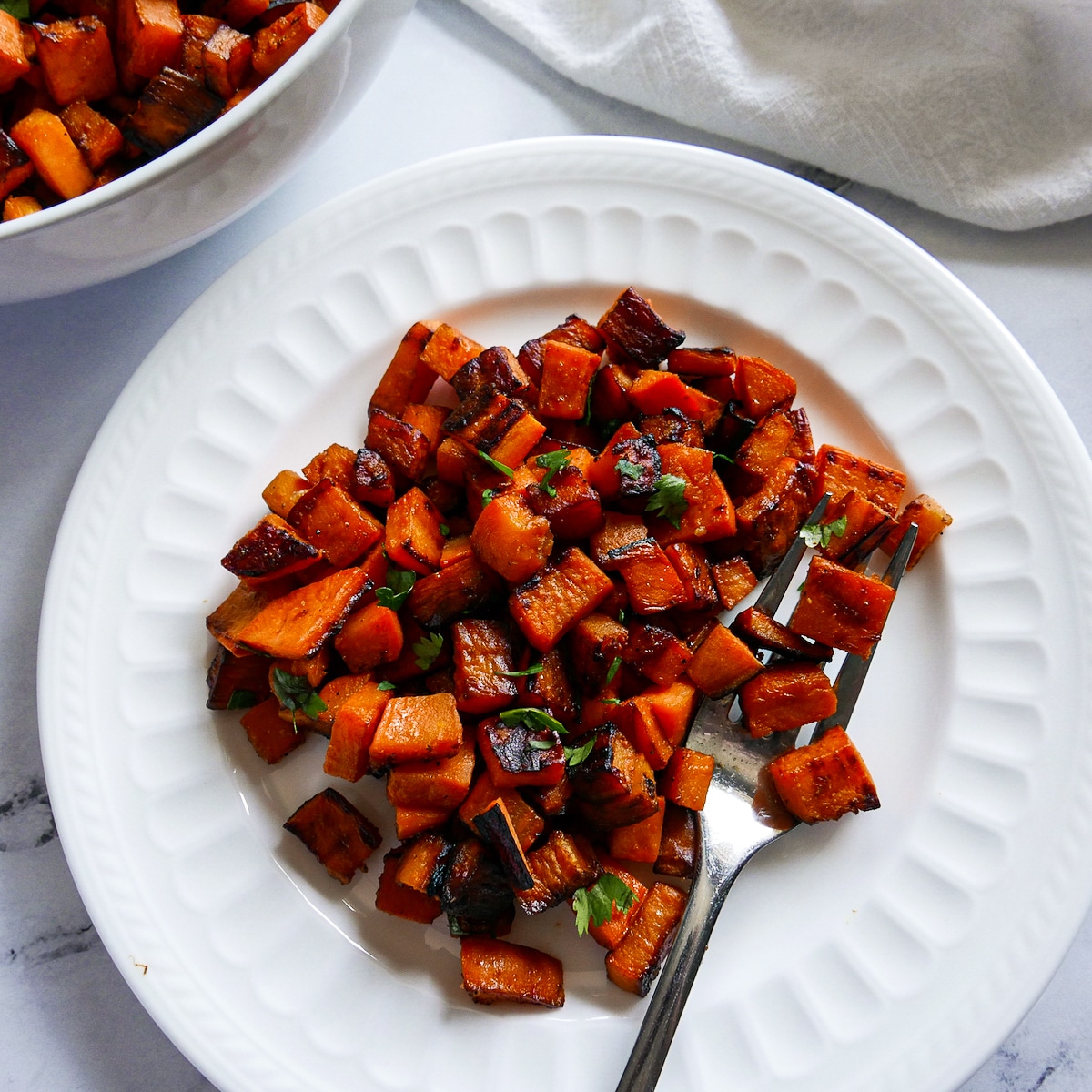 crispy potatoes on a white plate with fork and bowl of potatoes in the background. 