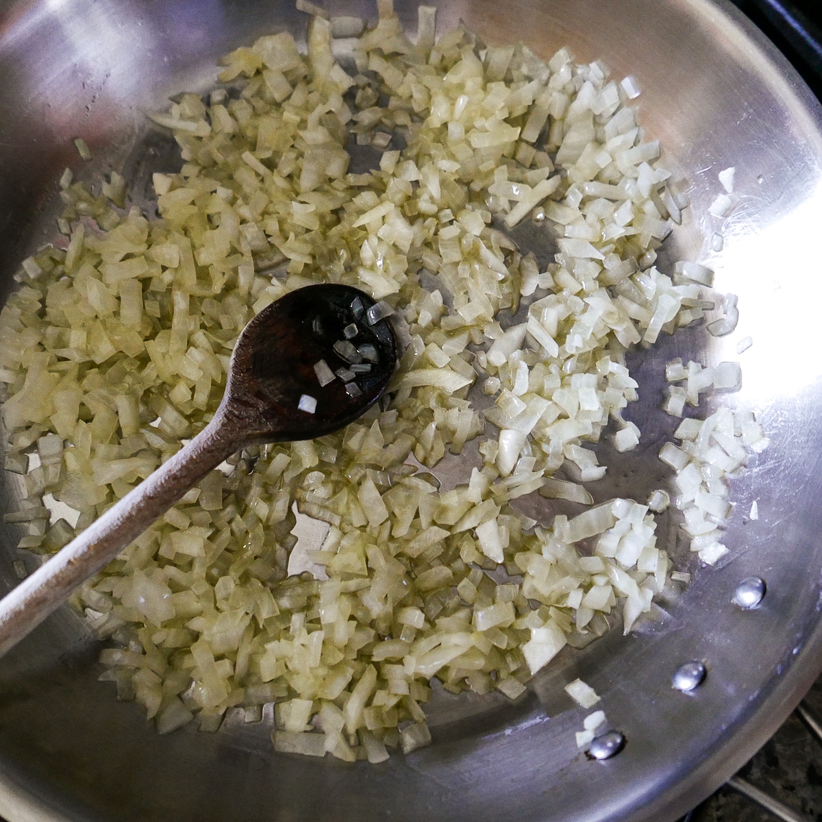 onions being sauteed in a large skillet with a wooden spoon.