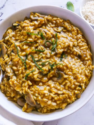 bowl of risotto with a spoon, white napkin, and sage leaves.