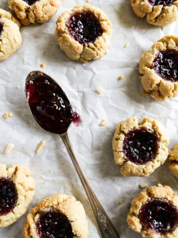 thumbprint cookies arranged on parchment paper with a spoon full of jam.