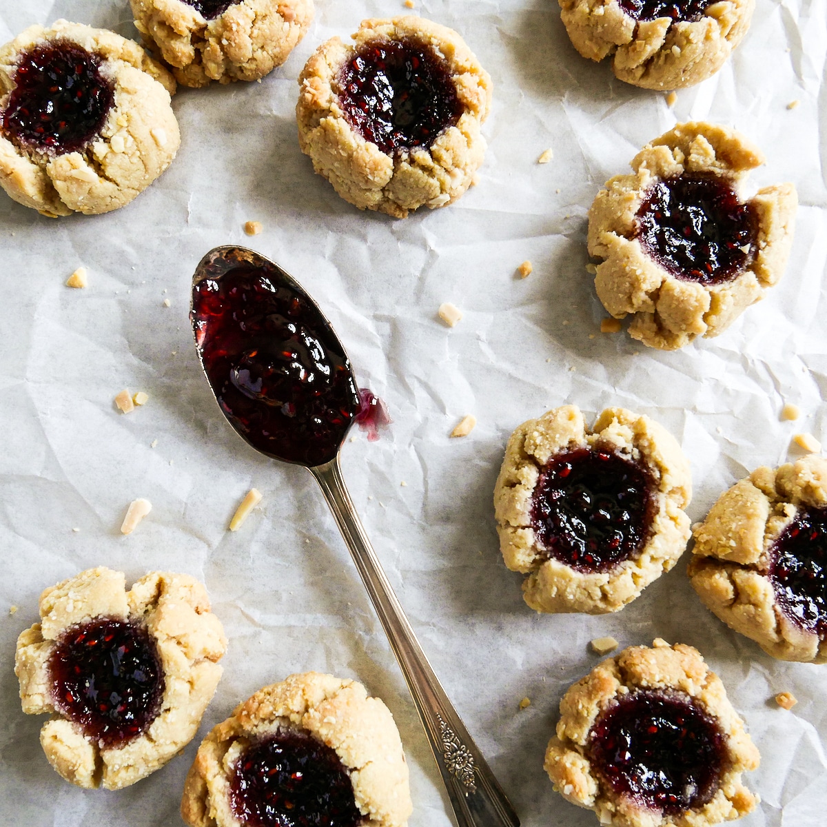 cookies-on-parchment.jpg thumbprint cookies arranged on parchment paper with a spoon full of jam.