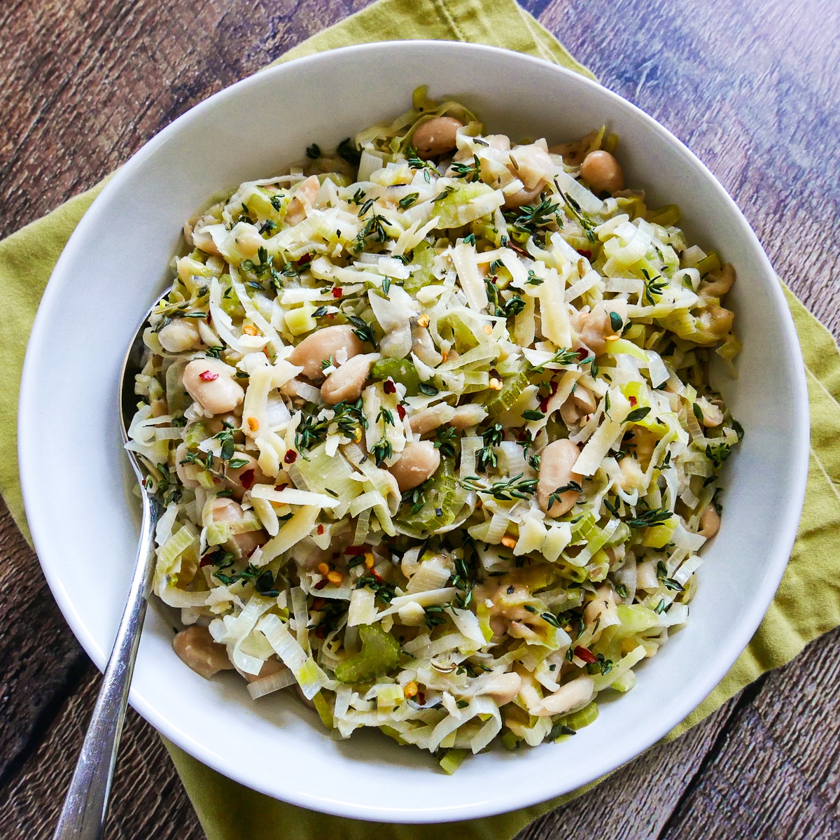 bowl of creamy braised white beans and leeks with a spoon.