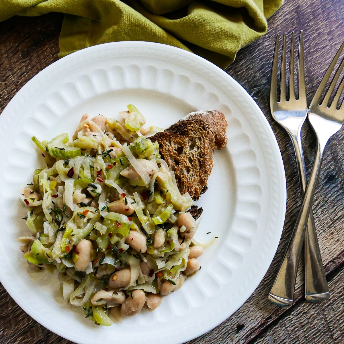 braised-beans-on-toast.jpg braised beans on toast arranged on a white plate with two forks nearby.