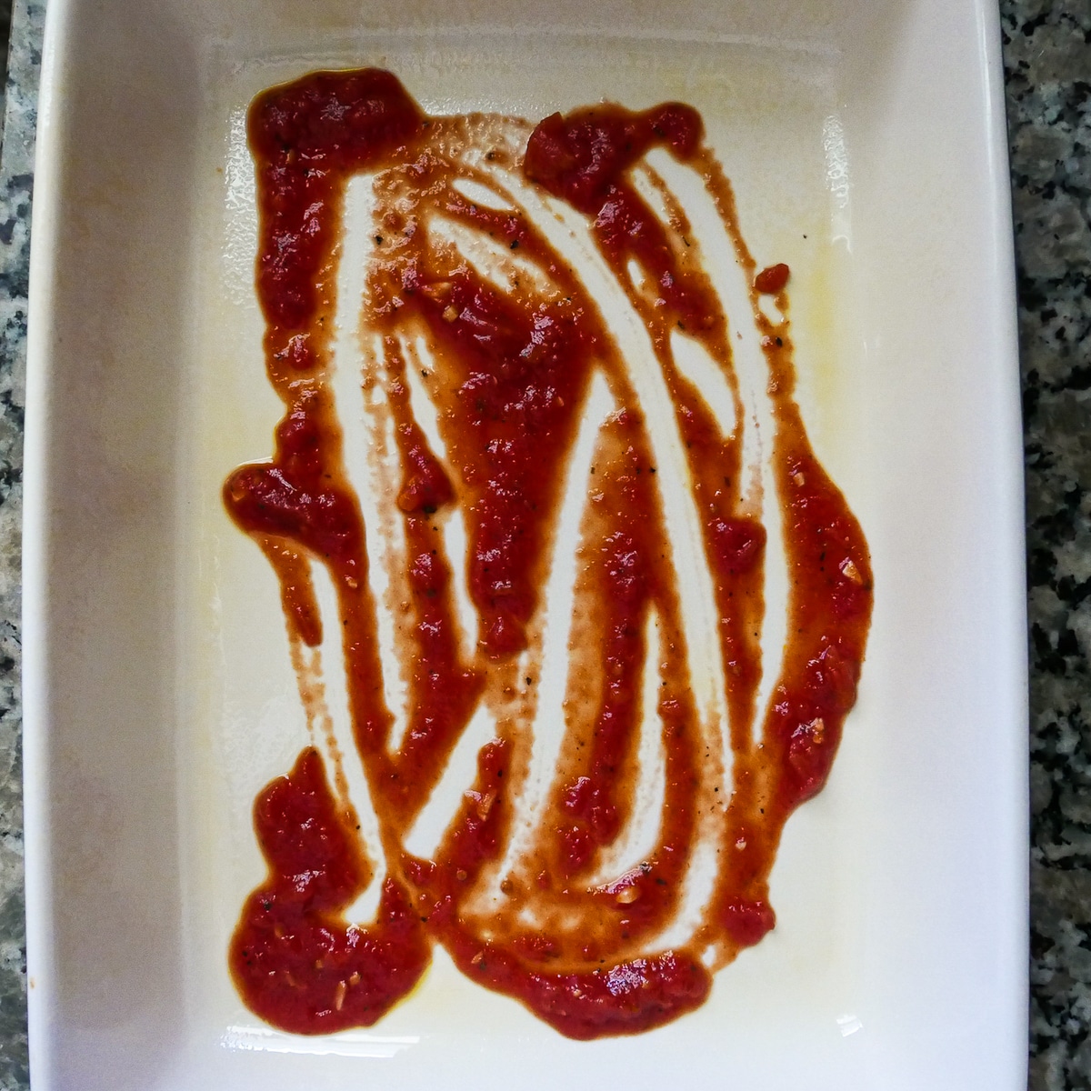 tomato-sauce-in-baking-dish.jpg A small amount of tomato sauce spread evenly on bottom of prepared baking dish.