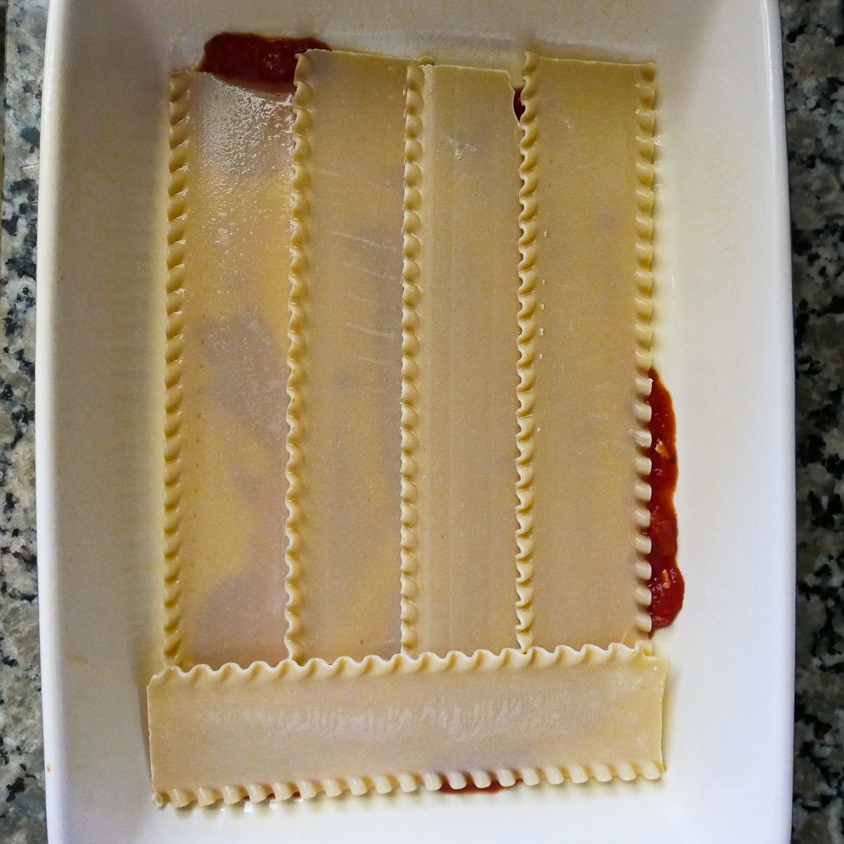 lasagna-noodles-in-baking-dish.jpg soaked lasagna noodles on top of sauce in baking dish.