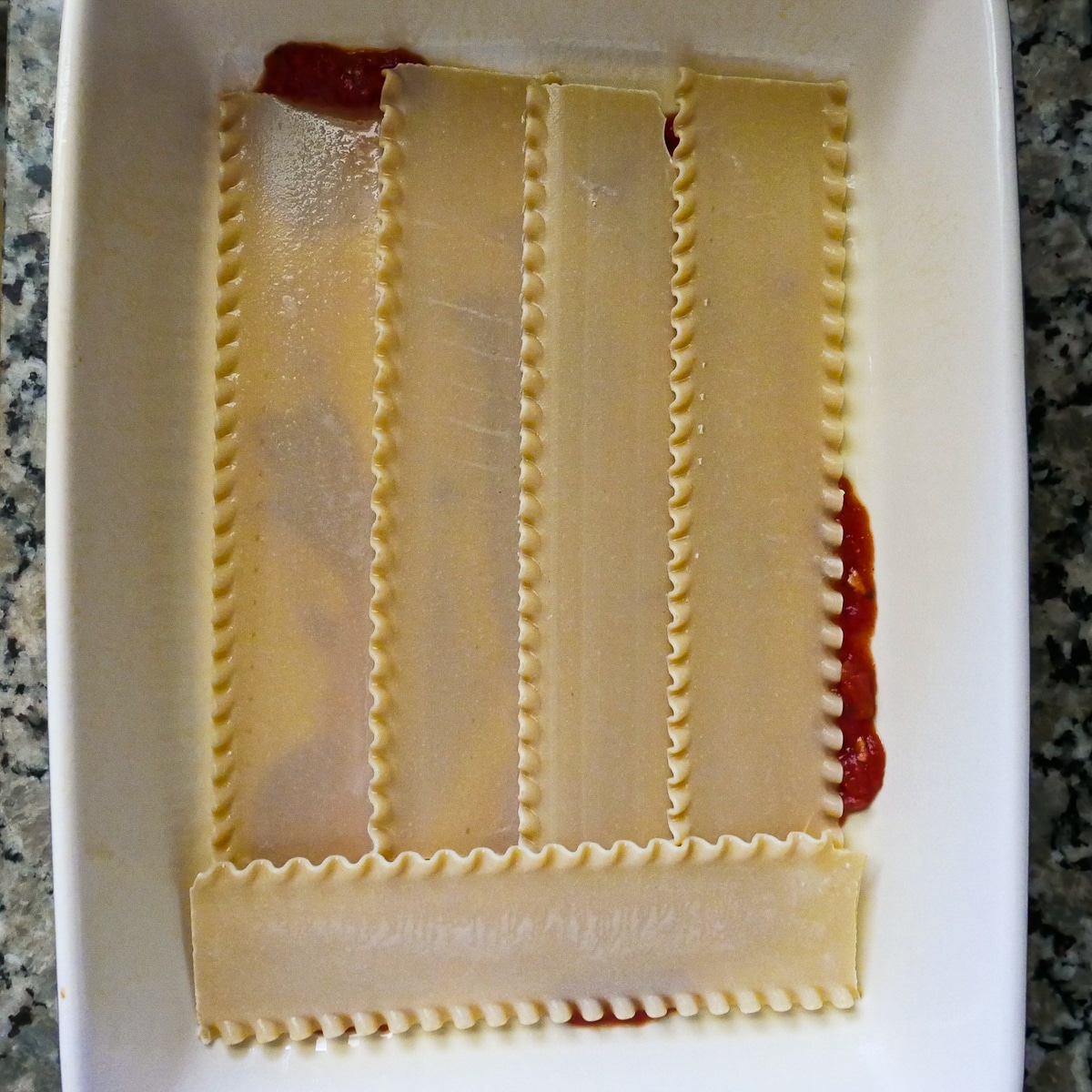 soaked lasagna noodles on top of sauce in baking dish.