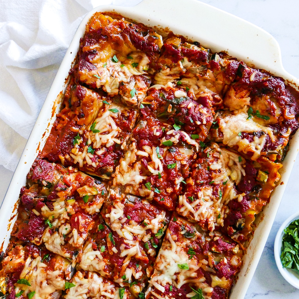 pan-of-lasagna.jpg vegetarian lasagna in a baking dish with a white napkin and fresh parsley.