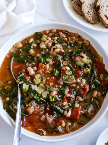 bowl of black eyed pea soup with a spoon and plate of bread.
