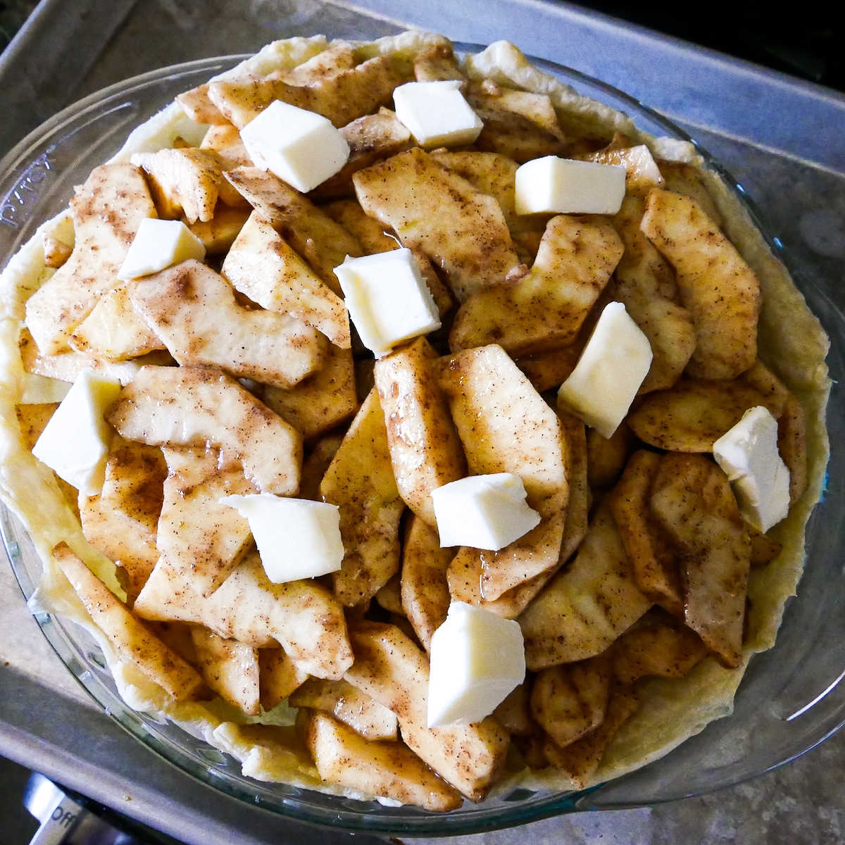 butter-on-apple-mixture.jpg pieces of butter placed on top of apple mixture in a pie dish.