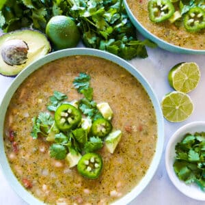 bowl of vegetarian white bean chili garnished with fresh cilantro, avocado, and sliced jalapenos.