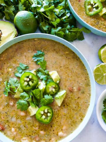 bowl of vegetarian white bean chili garnished with fresh cilantro, avocado, and sliced jalapenos.