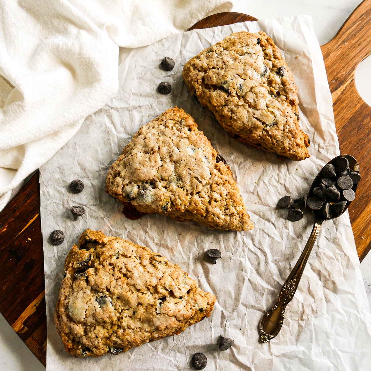three scones on a parchment lined cutting board with spoonful of chocolate chips. 
