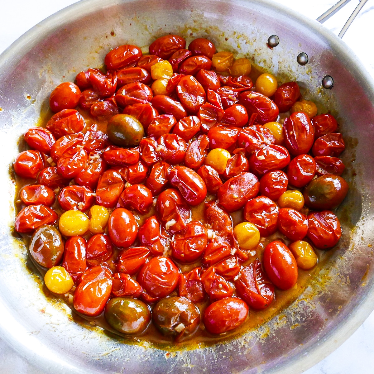 cherry tomatoes being cooked in a large skillet with garlic.