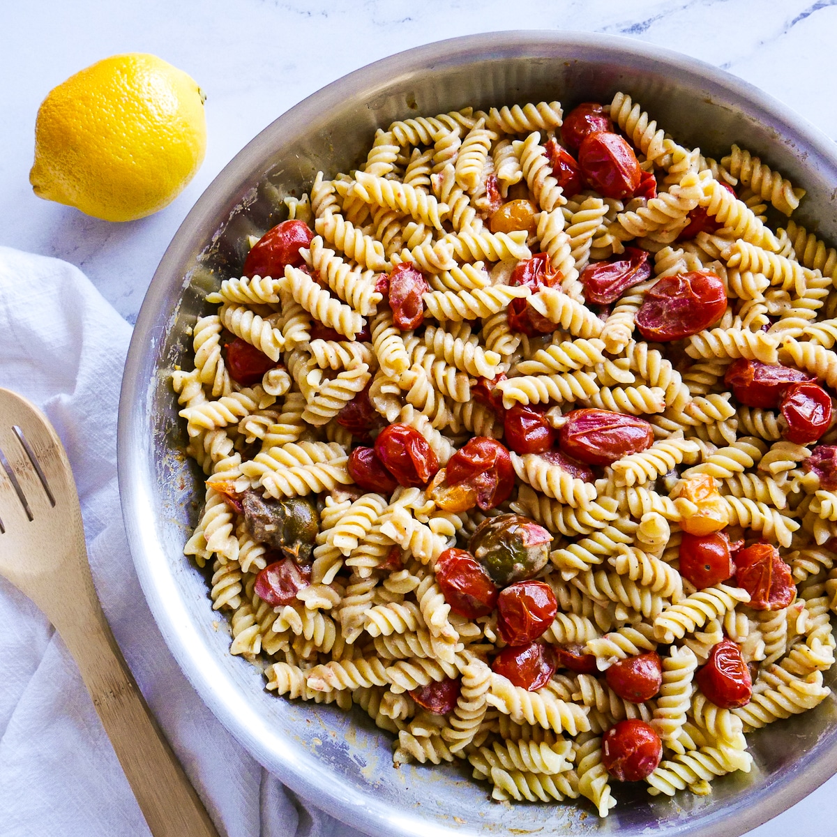 pasta and tahini sauce added to skillet with cherry tomatoes. 