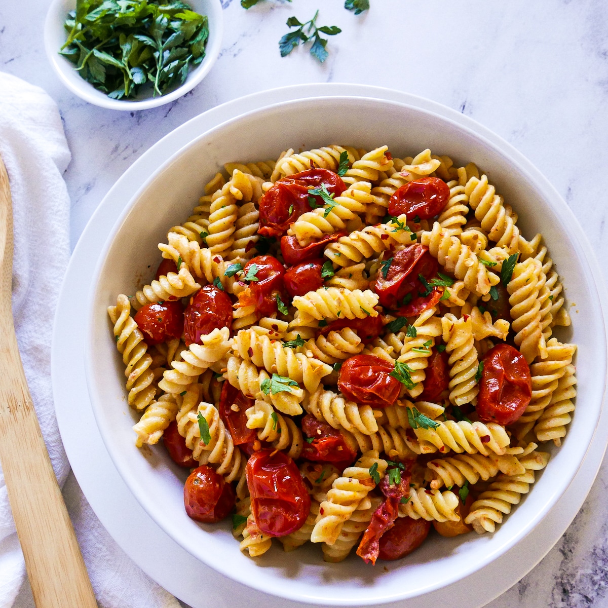 bowl of pasta with tahini sauce and cherry tomatoes resting on a plate.