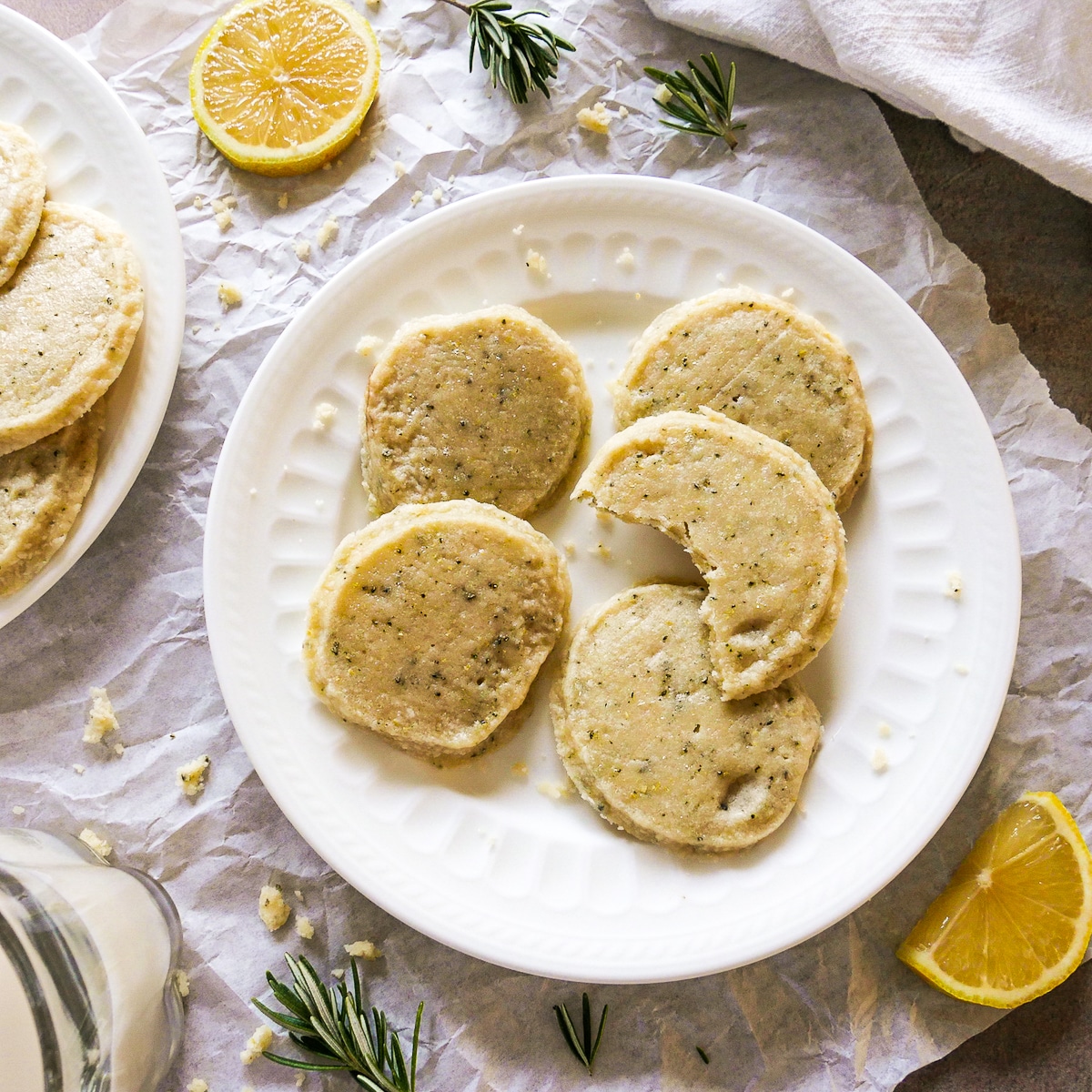 Rosemary lemon shortbread on a plate with rosemary sprigs and sliced lemon.