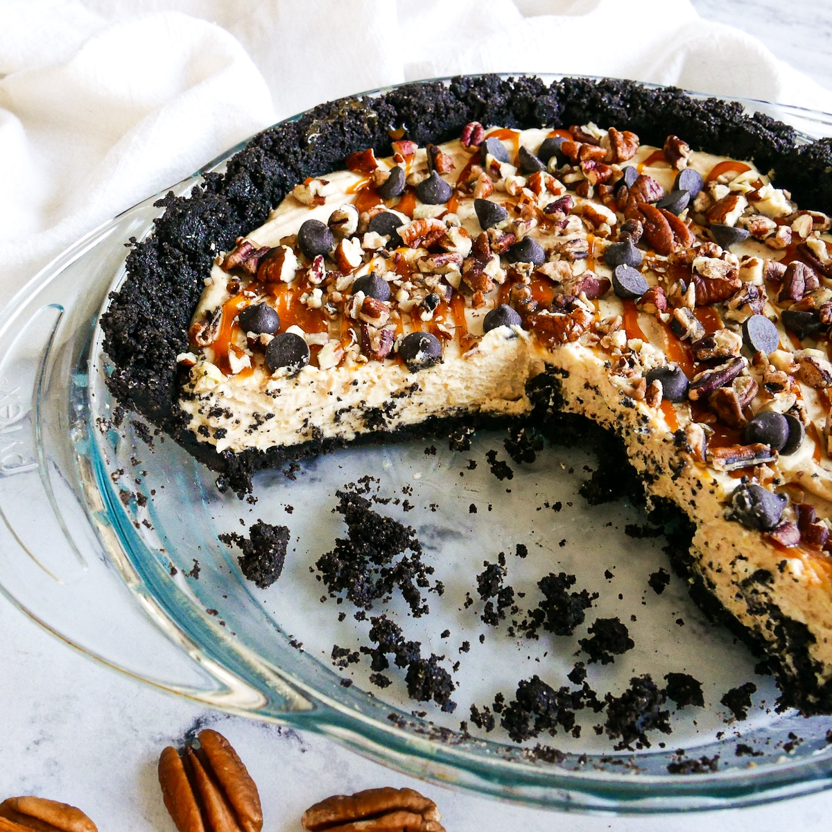 caramel chocolate pie that has been cut into with cookie crumbs in pie pan.