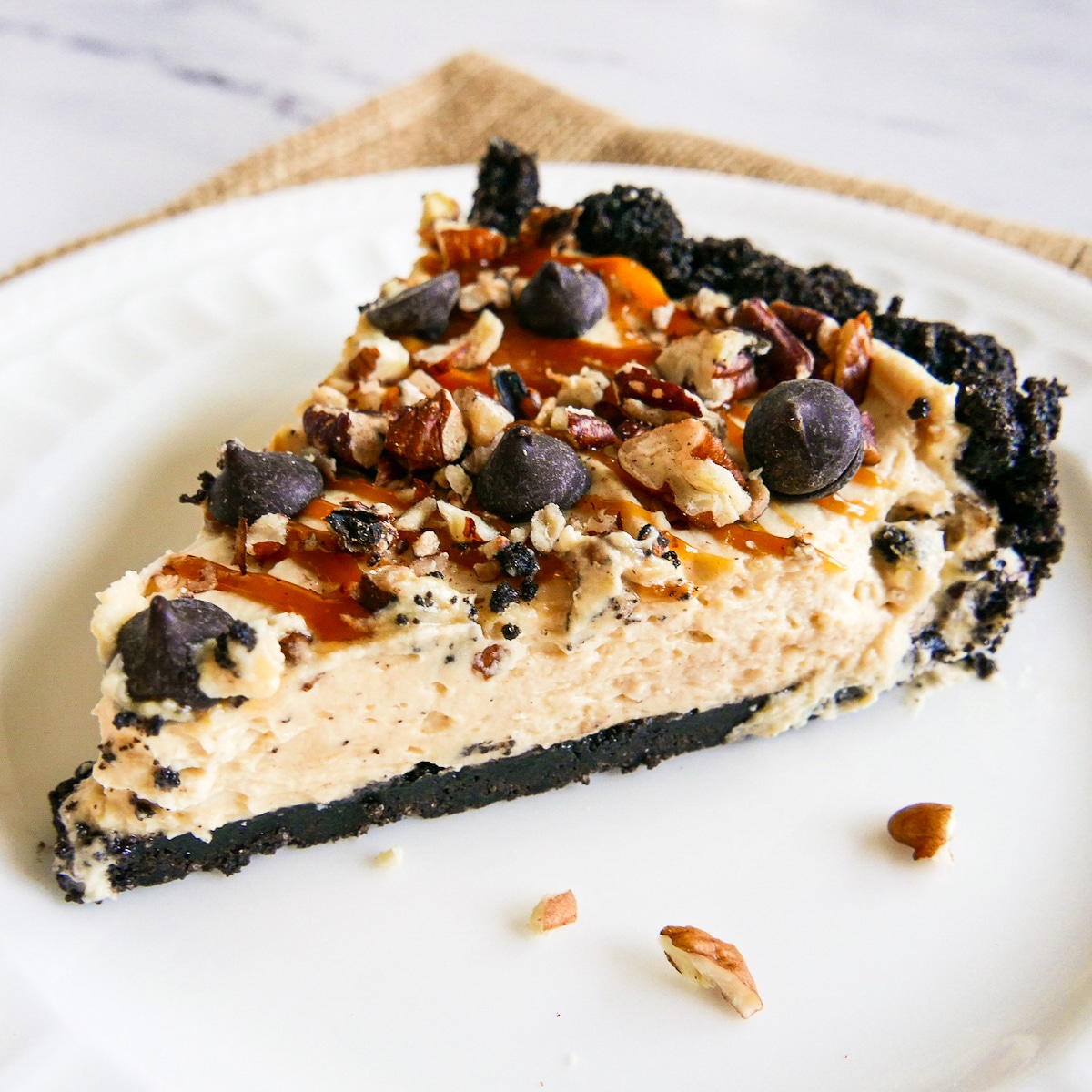 slice of pecan turtle pie on a white plate with chopped pecans.