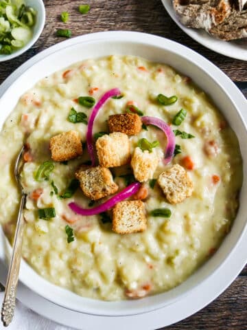 bowl of potato soup garnished with scallions, parsley, and pickled onions.