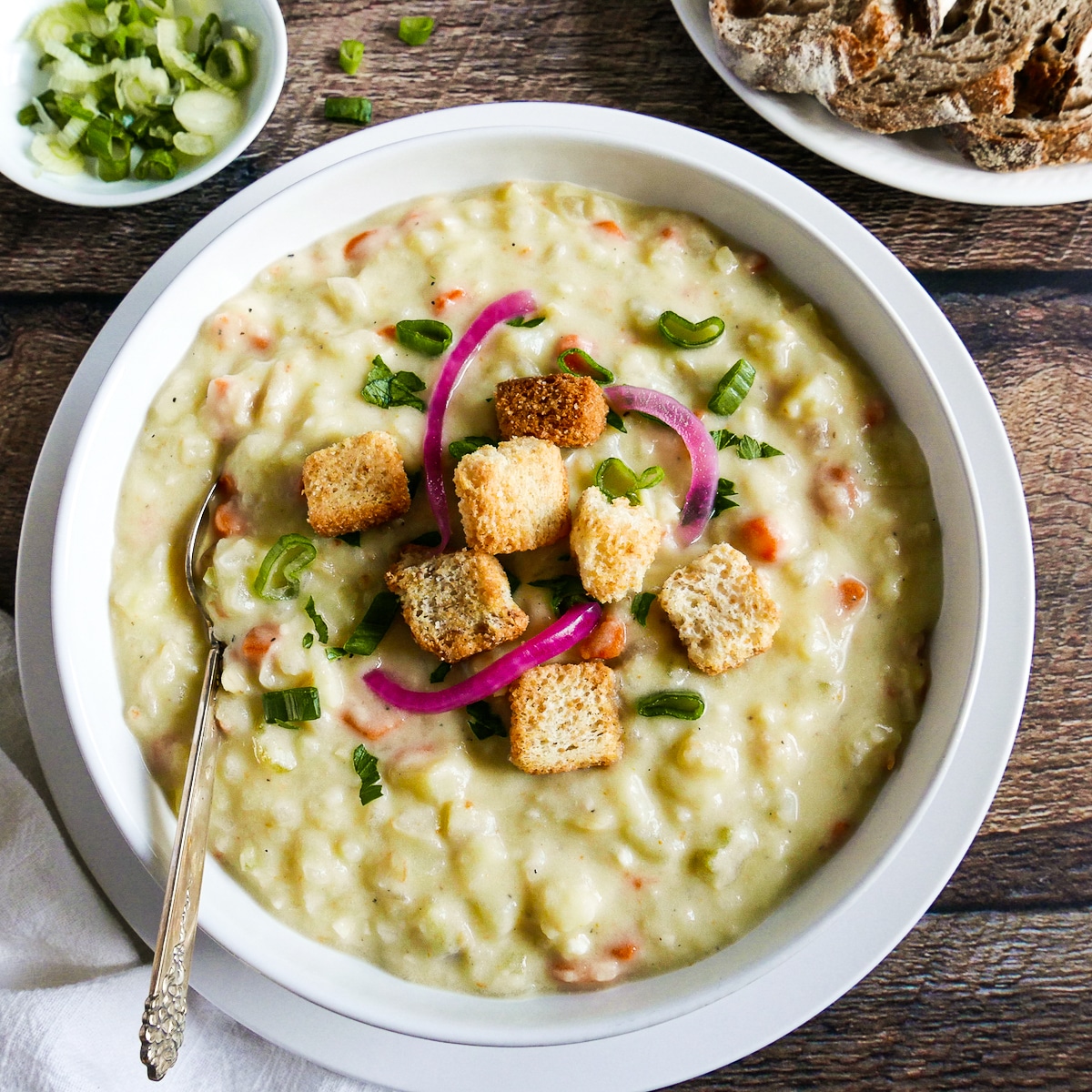 bowl of potato soup garnished with scallions, parsley, and pickled onions.