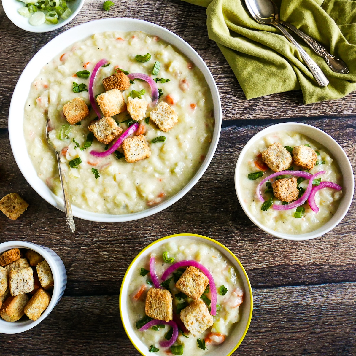 three bowls of potato soup with spoons and a green napkin.