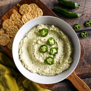 bowl of jalapeno artichoke dip arranged on a cutting board with crackers.