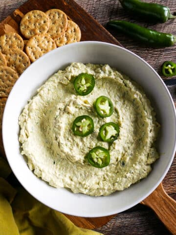 bowl of jalapeno artichoke dip arranged on a cutting board with crackers.
