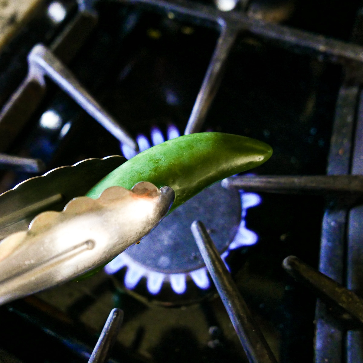 tongs holding a jalapeno over an open flame.