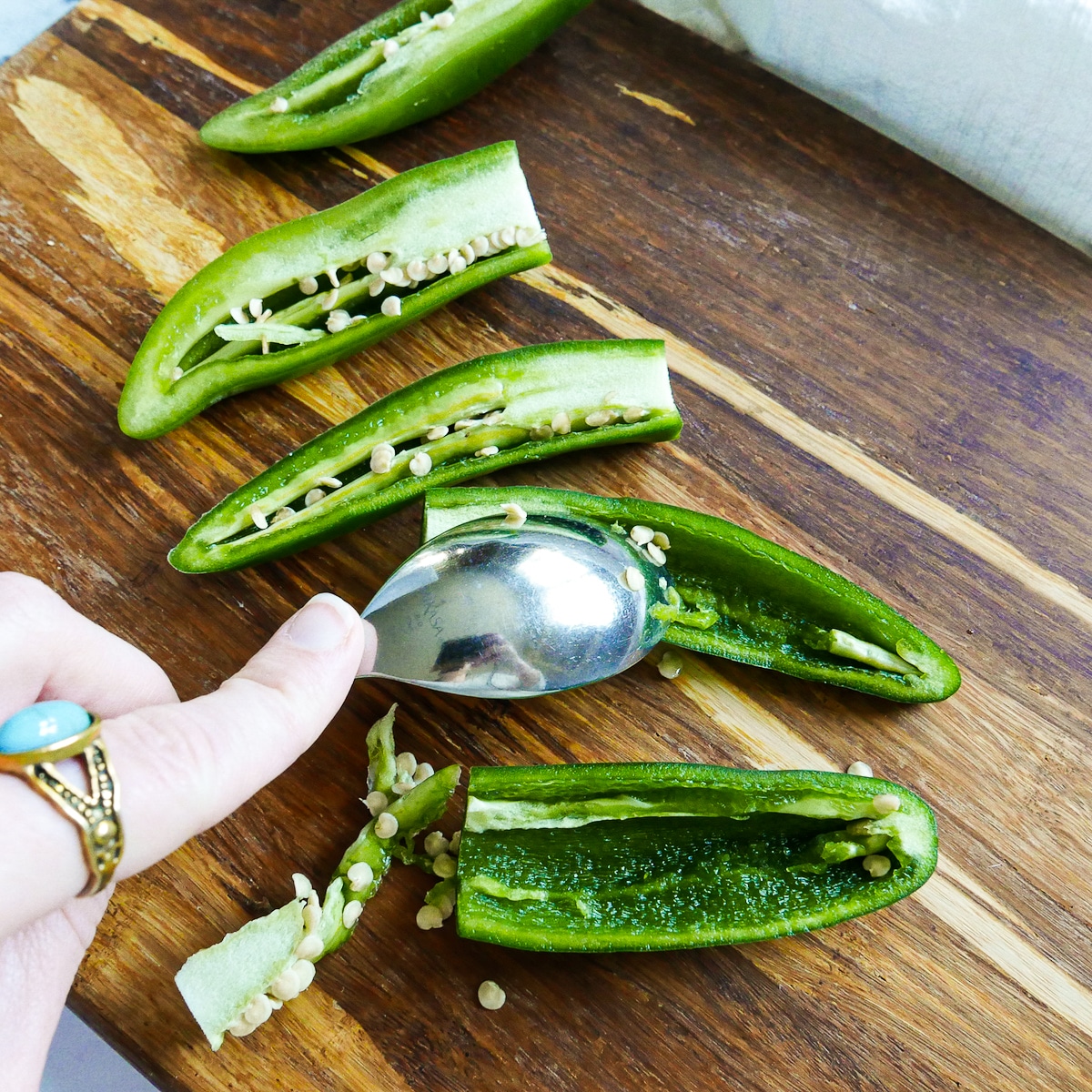 seeding jalapenos with a spoon on a cutting board. 