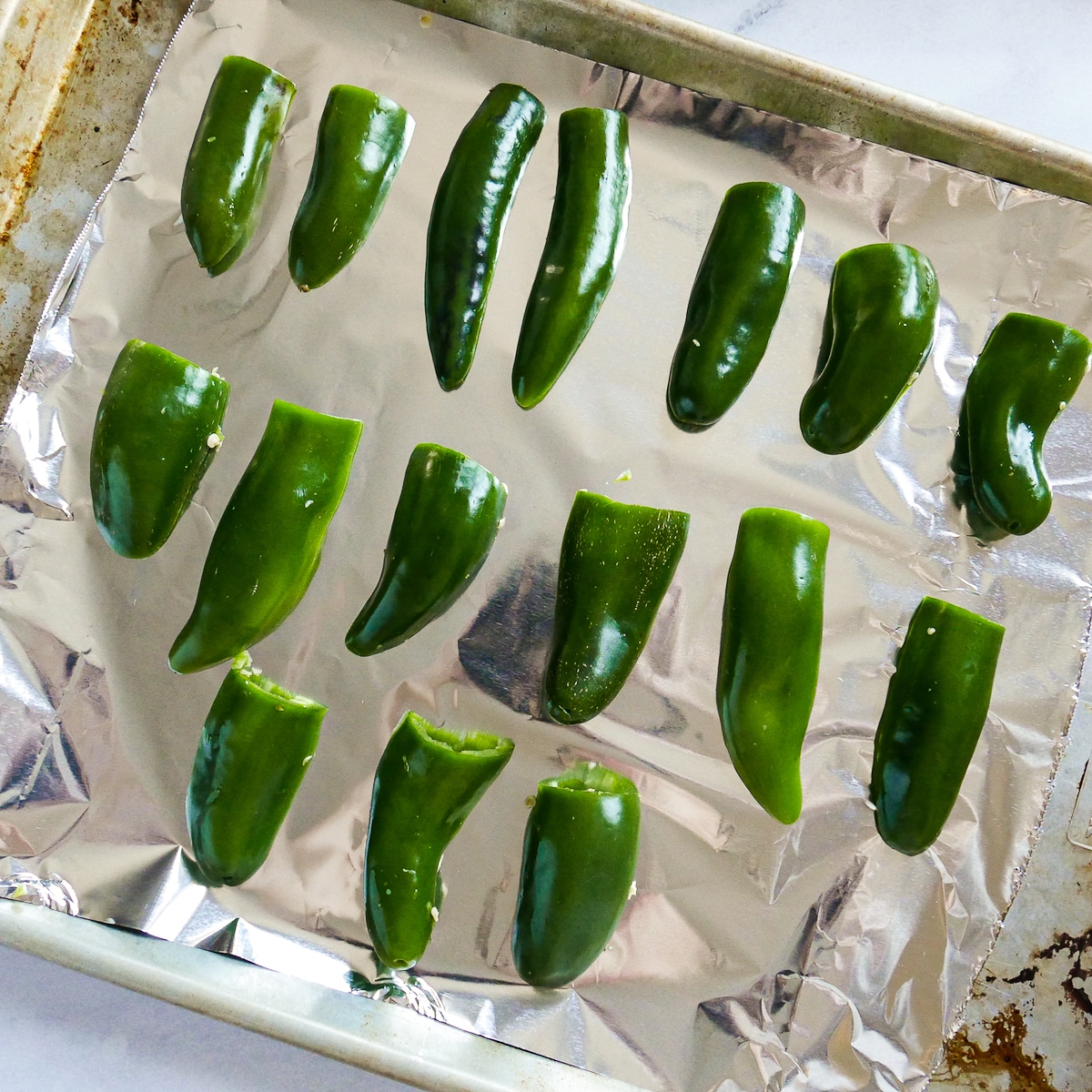 sliced jalapenos arranged on a foil-lined baking sheet.