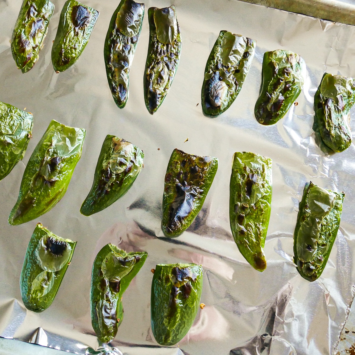 charred and blistered jalapenos on a foil-lined baking sheet.