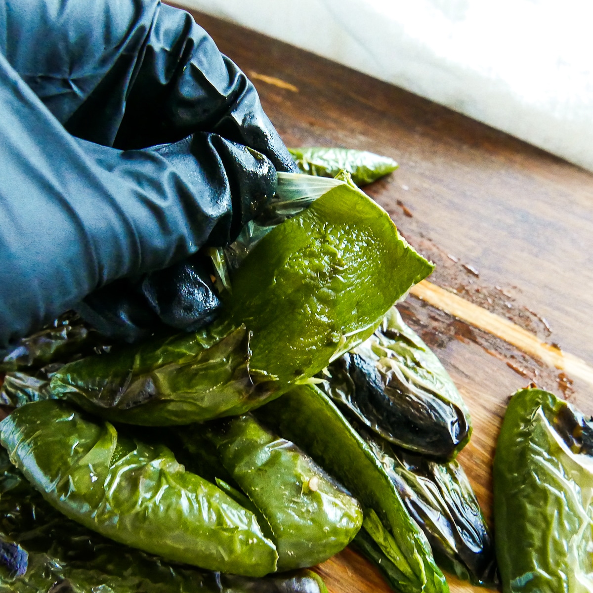 gloved hand peeling skin off of jalapenos. 
