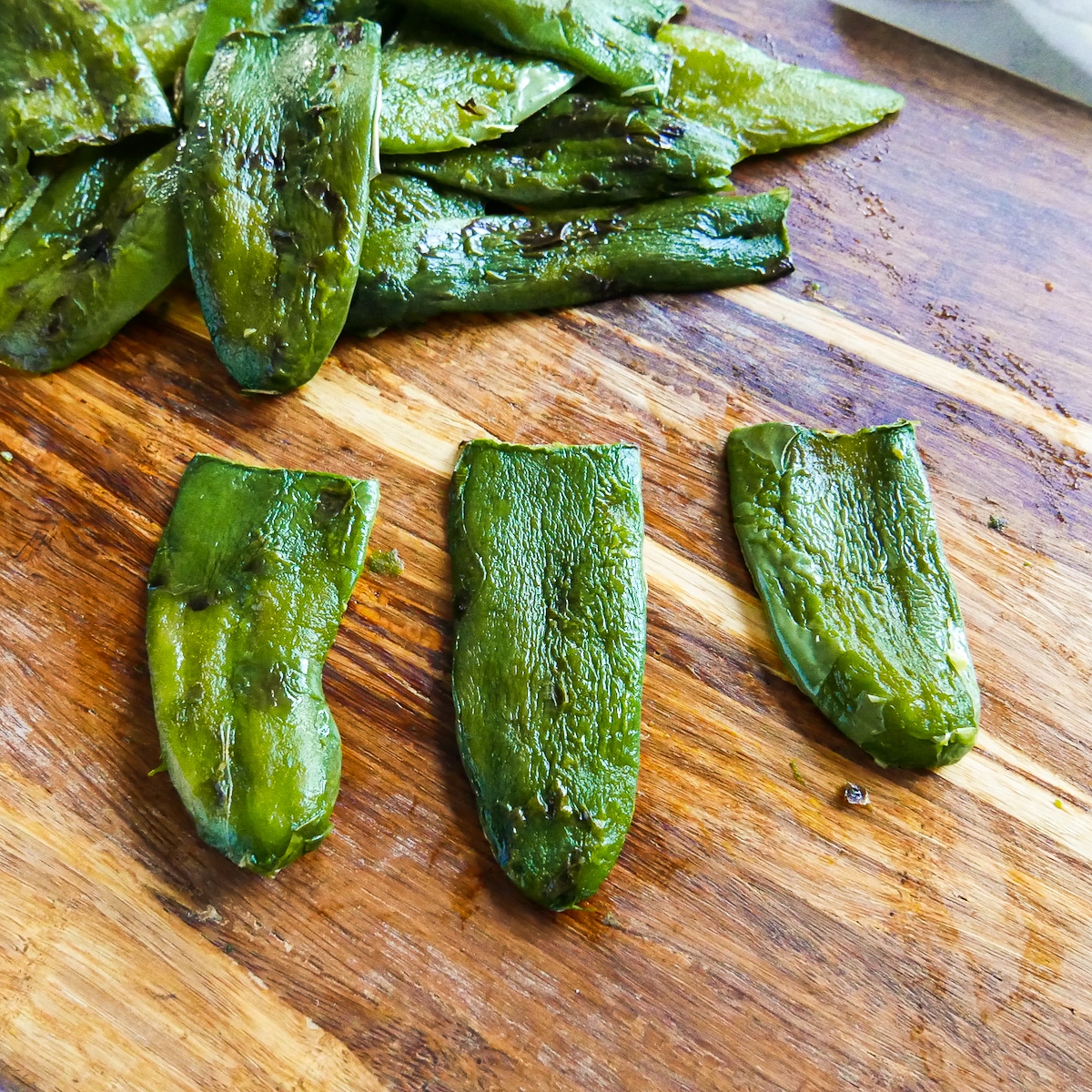 three roasted jalapenos arranged on a cutting board.