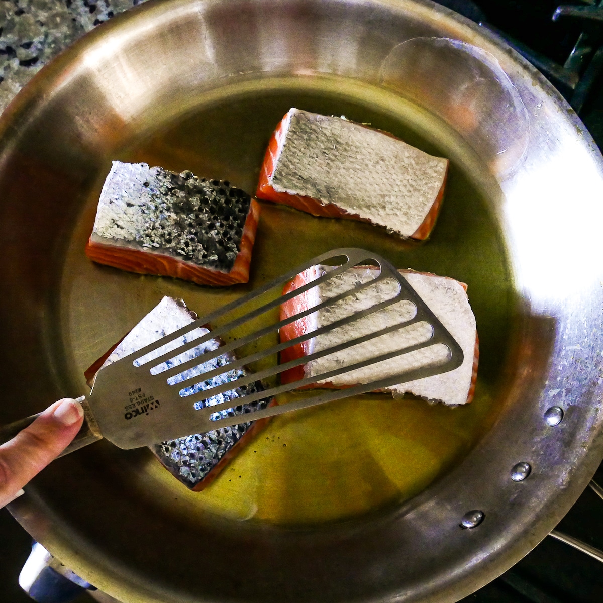 four fillets of salmon cooking in large frying pan.