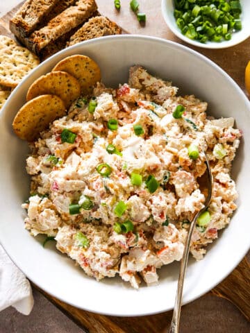 bowl of imitation crab dip with spoon and crackers.