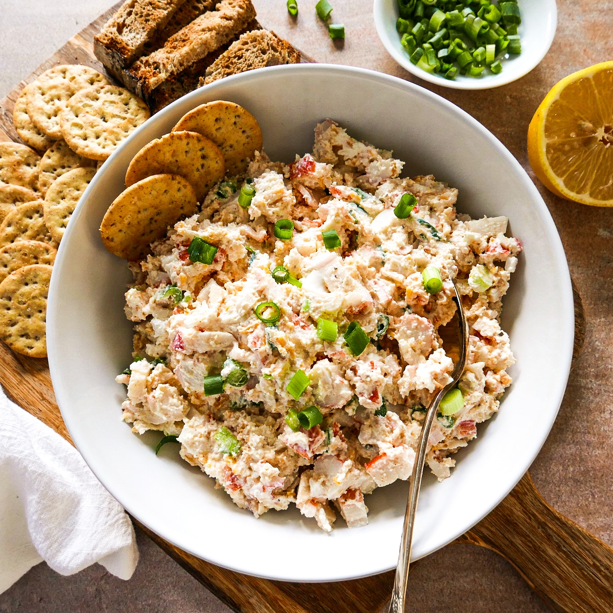 bowl of imitation crab dip with spoon and crackers.