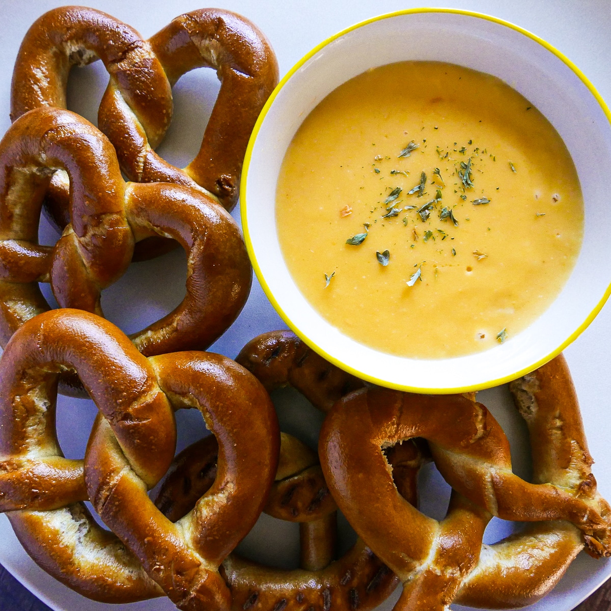 cheese dip for pretzels in a white bowl garnished with parsley.