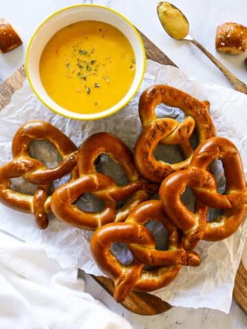 bowl of pretzel cheese dip with soft pretzels on a cutting board.