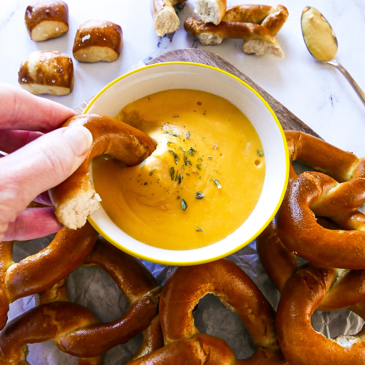 white hand dipping a piece of pretzel into cheese sauce.