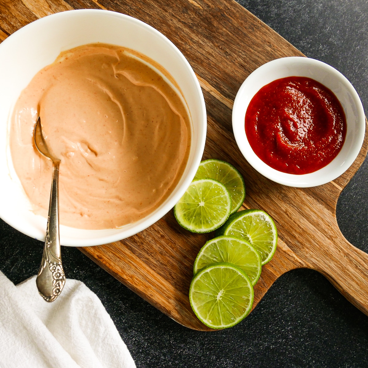 bowl-of-homemade-aioli.jpg bowl of creamy sriracha sauce with fresh limes on a cutting board.