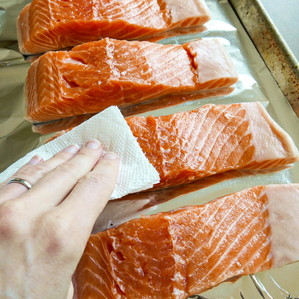 white hand patting salmon fillets dry with a paper towel. 